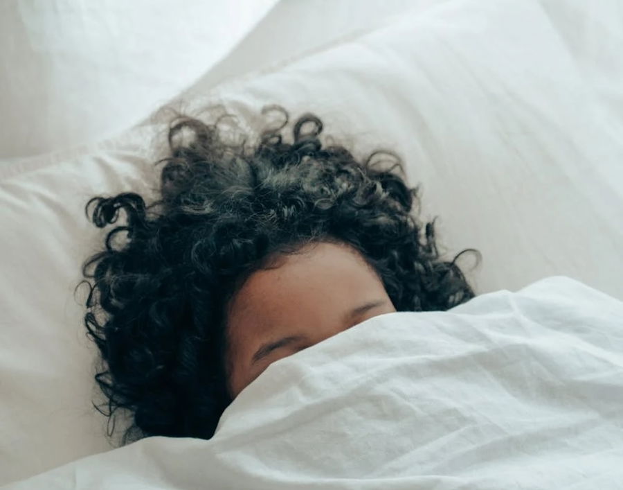 Woman in bed with blanket over her face